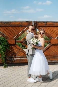 young couple bride in a white short dress and groom in a gray suit near the wooden rural gate of the estate