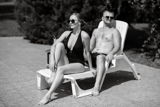 guy and a girl in bathing suits are relaxing, sunbathing and having fun near the blue pool