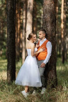 young couple bride in a white short dress and groom in a gray suit in a pine forest among the trees