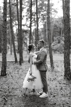 young couple bride in a white short dress and groom in a gray suit in a pine forest among the trees