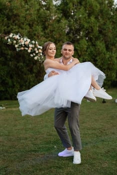 the first dance of the groom and bride in a short wedding dress on a green meadow