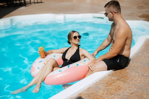 guy and a girl in bathing suits are relaxing, sunbathing and having fun near the blue pool