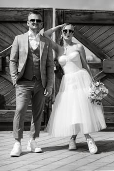 young couple bride in a white short dress and groom in a gray suit near the wooden rural gate of the estate