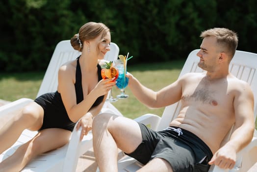 guy and a girl in bathing suits are relaxing, sunbathing and having fun near the blue pool