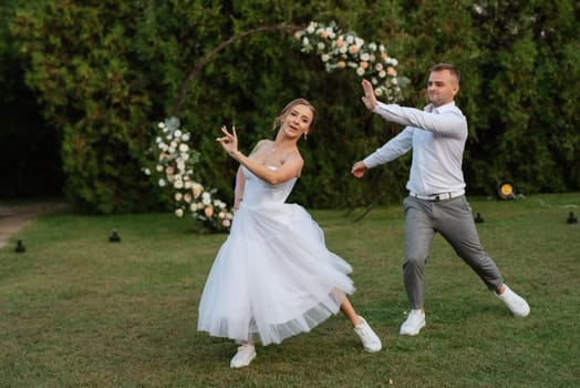 the first dance of the groom and bride in a short wedding dress on a green meadow