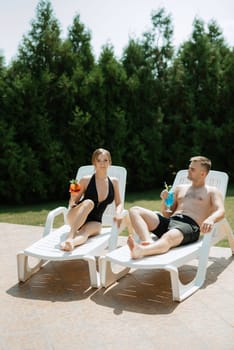 guy and a girl in bathing suits are relaxing, sunbathing and having fun near the blue pool