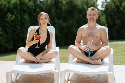 guy and a girl in bathing suits are relaxing, sunbathing and having fun near the blue pool