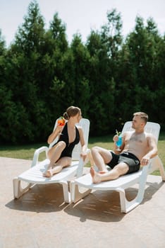 guy and a girl in bathing suits are relaxing, sunbathing and having fun near the blue pool