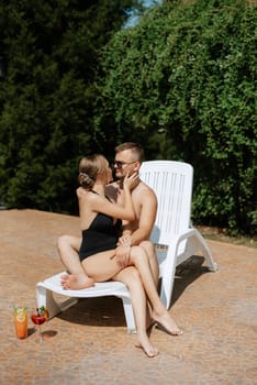 guy and a girl in bathing suits are relaxing, sunbathing and having fun near the blue pool