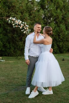 the first dance of the groom and bride in a short wedding dress on a green meadow