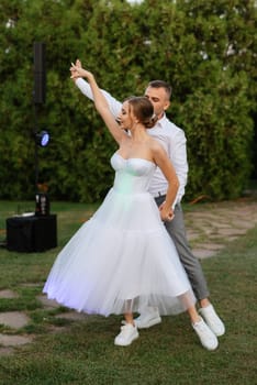 the first dance of the groom and bride in a short wedding dress on a green meadow