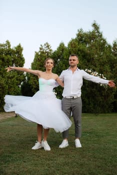 the first dance of the groom and bride in a short wedding dress on a green meadow