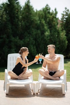 guy and a girl in bathing suits are relaxing, sunbathing and having fun near the blue pool