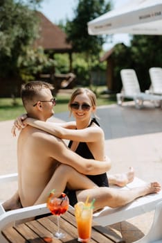 guy and a girl in bathing suits are relaxing, sunbathing and having fun near the blue pool