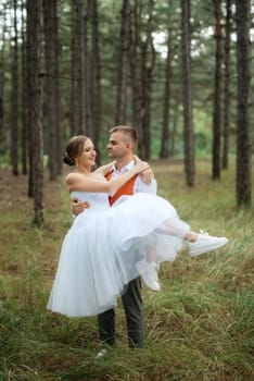 young couple bride in a white short dress and groom in a gray suit in a pine forest among the trees