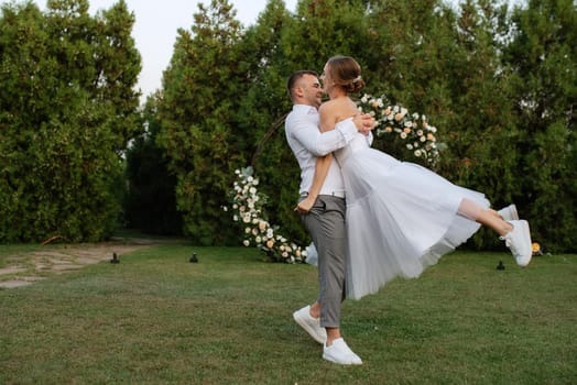 the first dance of the groom and bride in a short wedding dress on a green meadow