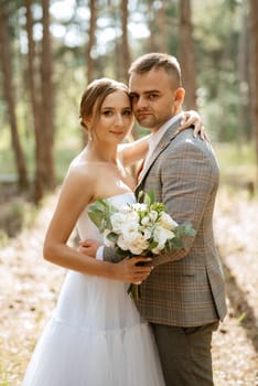 young couple bride in a white short dress and groom in a gray suit in a pine forest among the trees