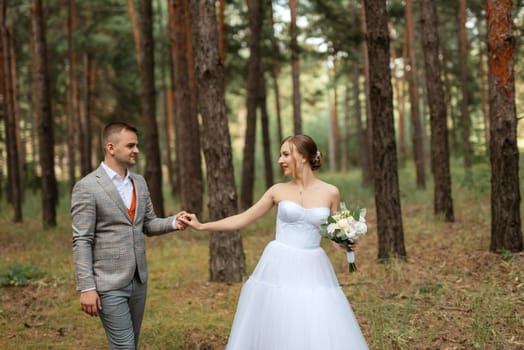 young couple bride in a white short dress and groom in a gray suit in a pine forest among the trees