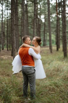 young couple bride in a white short dress and groom in a gray suit in a pine forest among the trees