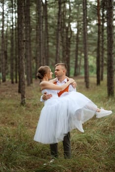 young couple bride in a white short dress and groom in a gray suit in a pine forest among the trees