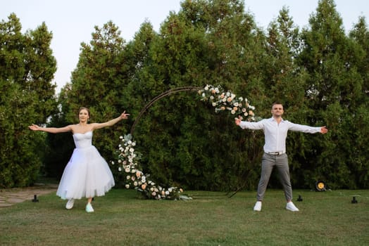 the first dance of the groom and bride in a short wedding dress on a green meadow