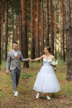 young couple bride in a white short dress and groom in a gray suit in a pine forest among the trees