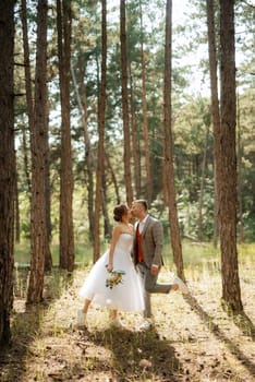 young couple bride in a white short dress and groom in a gray suit in a pine forest among the trees