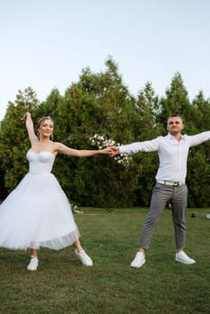 the first dance of the groom and bride in a short wedding dress on a green meadow