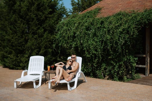 guy and a girl in bathing suits are relaxing, sunbathing and having fun near the blue pool