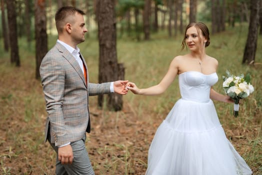 young couple bride in a white short dress and groom in a gray suit in a pine forest among the trees