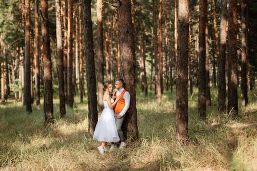 young couple bride in a white short dress and groom in a gray suit in a pine forest among the trees