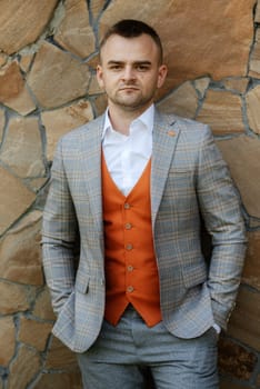 portrait of the groom in a gray suit and an orange vest and white sneakers