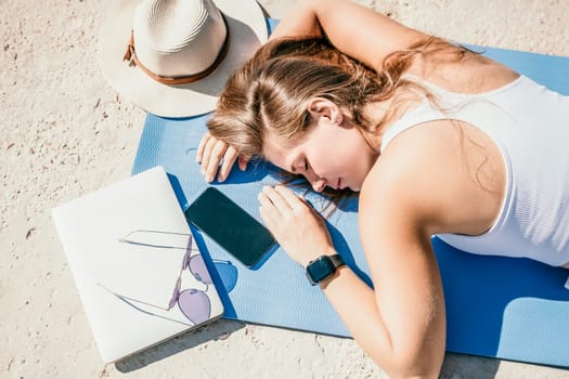 Successful business woman in yellow hat working on laptop by the sea. Pretty lady typing on computer at summer day outdoors. Freelance, travel and holidays concept.