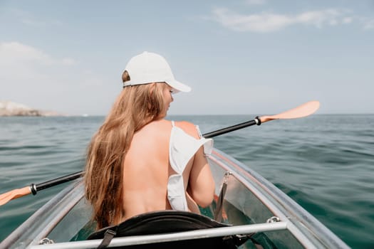 Woman in kayak back view. Happy young woman with long hair floating in transparent kayak on the crystal clear sea. Summer holiday vacation and cheerful female people having fun on the boat.
