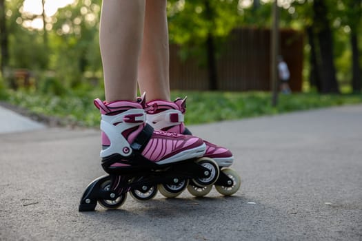 Spending time in a green city park. Close-up of a woman's legs. Woman wearing rollerblades. Playing sports in a city park. A girl rollerblades on an asphalt alley.
