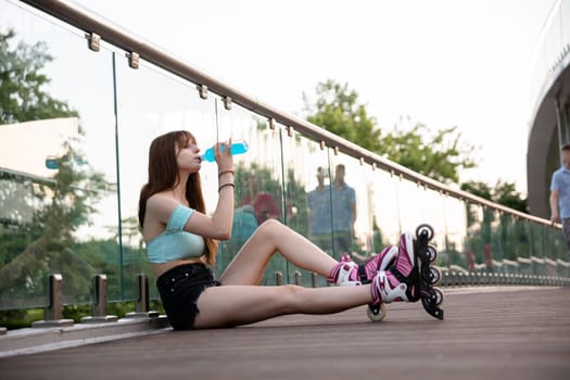 A woman wearing roller skates sits on a wooden bridge. A girl drinks a blue drink from a bottle. A long-haired brunette woman leans against a glass railing. The figure of a man walking is visible in the background.