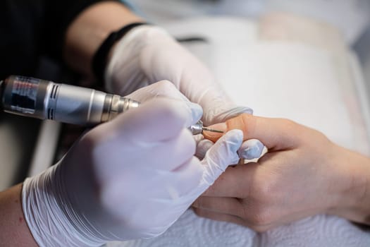 Close-up on the hands of a woman making a visit to a beauty salon. A professional beautician is giving a manicure on a natural nail plate. A girl with short nails has come in for a manicure