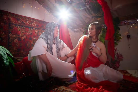 Portrait of young arabian muslim couple in traditional clothes in cozy red room. Fhoto shoot in easten style with male and female model like in harem with a sultan and an odalisque. Partial focus