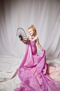 Portrait of cute kid girl posing in pink beautiful dress on white background. Young female model looking as magic princess from fairy taly