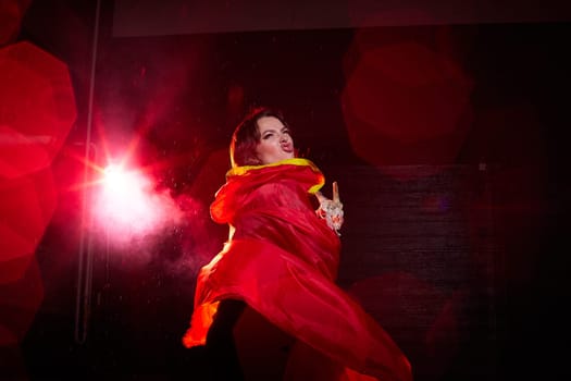 Witch woman in red cloak with skull on black background and light in night. Female warrior in Dark