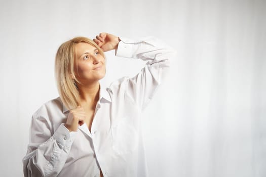 Portrait of a pretty blonde smiling woman posing on white background. Happy girl model in white shirt posing in studio. Copy space