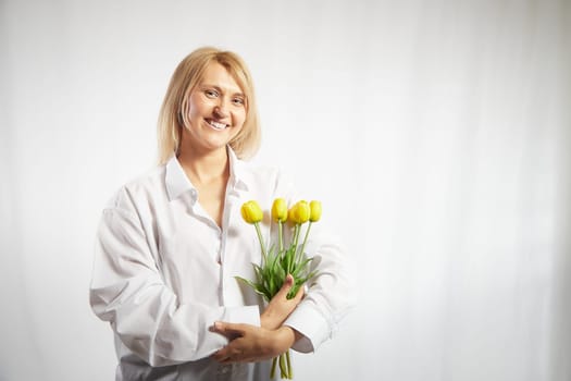 Beauty young blonde happy woman with bouquet of yellow tulips on white background. The concept of holiday and a gift for a lady and a girl. . Copy space