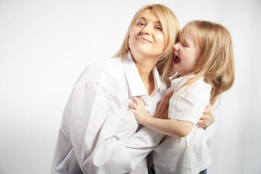 Portrait of a mother and daughter, where a little girl screams at an adult woman on a white background. The concept of a capricious child and behavior in family. Angry teen and calm lady