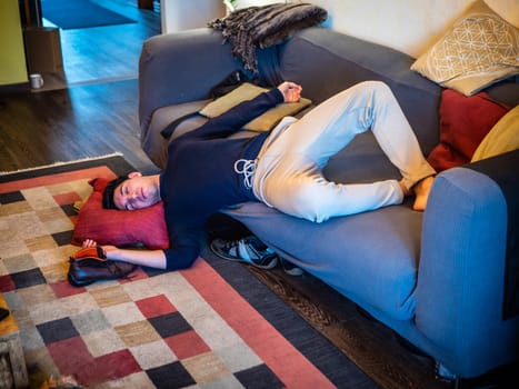 Drunk Young Handsome Man Resting on Couch in the Living Room with Head on the Floor.