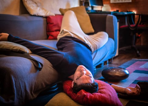 Drunk Young Handsome Man Resting on Couch in the Living Room with Head on the Floor.