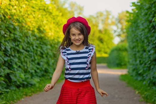 A portrait of a beautiful brunette in a red beret, red skirt, and a striped T-shirt runs among green leaves in the park. Copy space