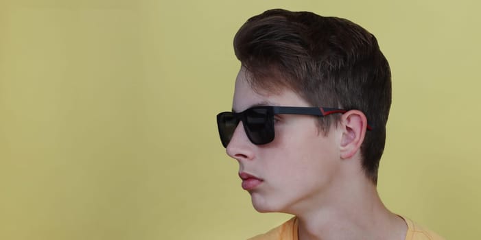 Closeup profile portrait of a teenage boy wearing black glasses. The face of a boy with glasses on a yellow background...