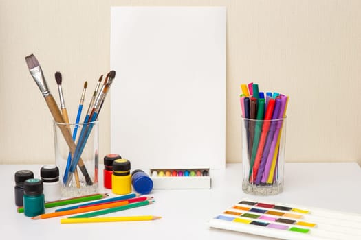 White paper, paintbrushes and colorful drawing supplies on white table: watercolors,pastel crayons, pencils , acrylic paints. Mock up