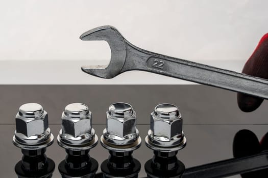 Shiny new wheel nuts and a wrench in the hand of a car mechanic on a dark background with reflection. Auto parts and auto repair. Car maintenance. copy space