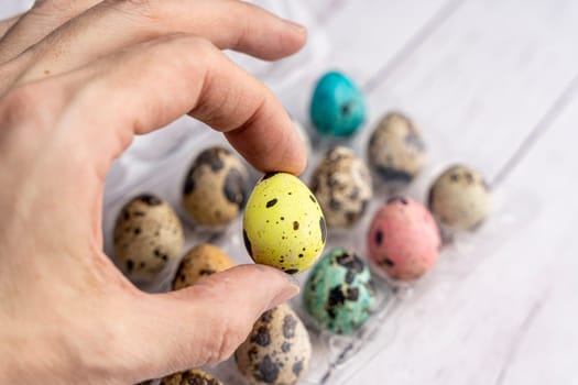 The hand holds a beautiful Easter egg. colorful Easter eggs in a container on a light background. Easter greeting card. a place to copy. close-up of quail eggs.